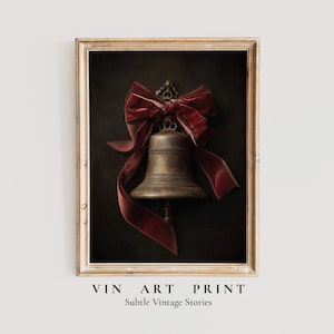 Puede incluir: Impresión artística enmarcada de una campana de bronce adornada con un gran lazo de terciopelo rojo oscuro sobre un fondo oscuro. La impresión tiene un marco dorado. El texto en la parte inferior dice "VIN ART PRINT" y "Subtle Vintage Stories."