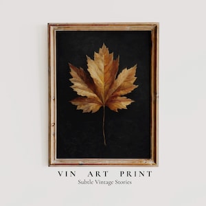 Puede incluir: Una impresión artística enmarcada que presenta una ilustración detallada de una hoja de arce en tonos marrones y dorados sobre un fondo negro. El marco es de color marrón claro y cálido. El texto en la parte inferior dice "VIN ART PRINT" y "Subtle Vintage Stories."