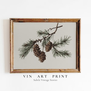 May include: A framed art print featuring a watercolor illustration of pine cones and evergreen branches. The artwork has a vintage aesthetic, with a neutral background and a warm-toned wooden frame. The text "VIN ART PRINT" and "Subtle Vintage Stories" are at the bottom.