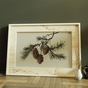 May include: A framed botanical print featuring a detailed illustration of a pine branch with green needles and brown pine cones. The frame is off-white with a marble-like pattern. The artwork is displayed on a wooden floor.