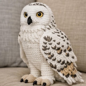 May include: A handcrafted, white crochet owl figurine with detailed wings and a black beak. The owl has yellow eyes and is perched on a neutral-toned surface. The wings feature brown and tan accents.
