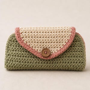 Puede incluir: Bolso de mano de ganchillo hecho a mano en tonos verdes, beige y rosa. El cuerpo principal es verde oliva, con una solapa beige delineada en rosa. Un botón de madera asegura la solapa. Este accesorio es ideal para llevar lo esencial.