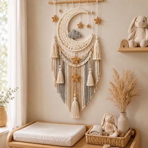 May include: A cream-colored macrame wall hanging in a nursery setting. The design features a crescent moon, stars, and tassels. The nursery also includes a changing table, a stuffed bunny, and decorative items.