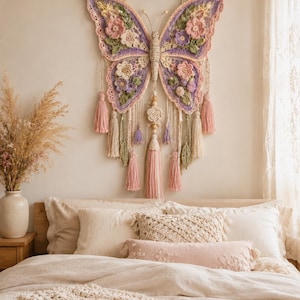 May include: A large, handcrafted crochet butterfly wall hanging in a bedroom setting. The butterfly is in shades of lavender, pink, and cream, with floral details. It has tassels and hangs from a wooden dowel, adding a bohemian touch to the bedroom decor.