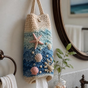 May include: A handmade crochet tissue holder in shades of beige, blue, and white, adorned with a pink starfish and seashell embellishments. The holder is designed to hang on a wall and has a button closure at the top.