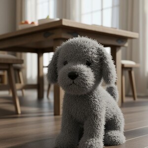 May include: A soft, grey plush puppy dog toy with floppy ears and a small tail. The stuffed animal is sitting on a wooden floor. A wooden table and chairs are in the background. The toy has a fuzzy texture.