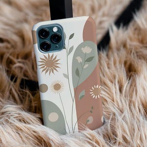 Op de afbeelding: Een telefoonhoesje met een bloemenontwerp. De hoes heeft een crèmekleurige achtergrond met abstracte vormen in bruin, groen en beige. Het ontwerp bevat gestileerde bloemen en bladeren. De hoes ligt op een zacht, lichtbruin oppervlak.