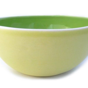 May include: A yellow ceramic bowl with a green interior. The bowl is round and has a smooth, glossy finish.