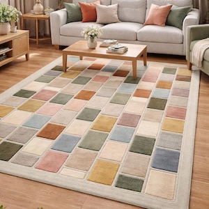 May include: A rectangular area rug with a geometric pattern of squares in various colors, including beige, pink, green, and blue. The rug has a light beige border and is placed on a hardwood floor. The rug is in a living room setting.