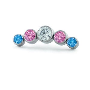 May include: A curved, silver-toned ear cuff featuring five round gemstones. The gemstones are in shades of blue, pink, and clear, set in individual bezels. The design is minimalist and elegant.