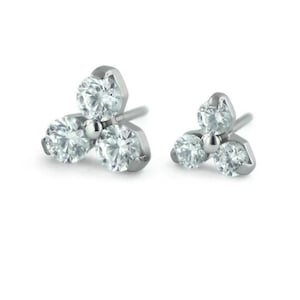 May include: Two silver-toned stud earrings, each featuring three clear, round-cut gemstones arranged in a triangular cluster. The earrings are set against a white background, highlighting their sparkle and design.