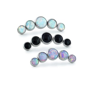 May include: Three curved rows of body jewelry. Each row features a series of round, bezel-set stones in varying colors. The top row has white and light blue stones. The middle row has black stones. The bottom row has purple and blue stones.