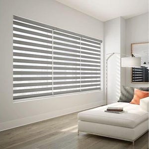 May include: A modern living room featuring gray and white horizontal striped window blinds. The blinds are installed in a large window, providing privacy and light control. The room also includes a white chaise lounge, a floor lamp, and artwork.