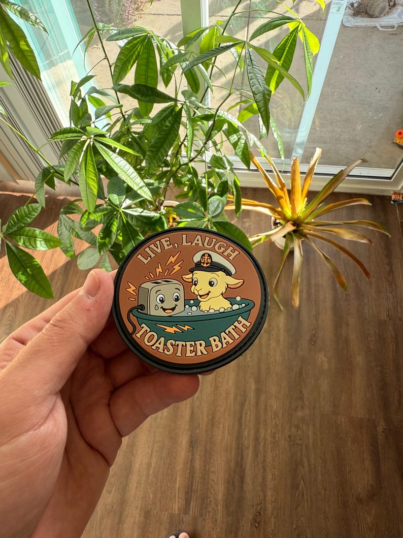 May include: A round patch with the words "LIVE, LAUGH" at the top and "TOASTER BATH" at the bottom. The patch features a cartoon toaster and a goat in a bathtub. The patch is brown, black, and tan.