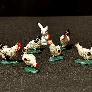 May include: A collection of miniature figurines featuring chickens and a rabbit. The chickens are white with black markings and red combs, standing on green bases. The rabbit is white and holding a carrot. The figurines are likely made of metal.