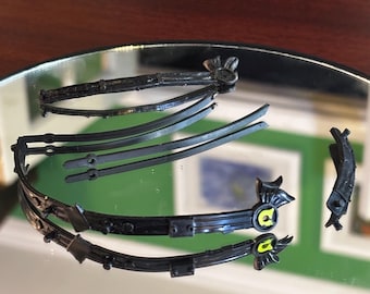 May include: Black plastic hair accessories, including headbands and decorative pieces. The headbands have ornate designs with yellow accents. The pieces are arranged on a reflective surface.