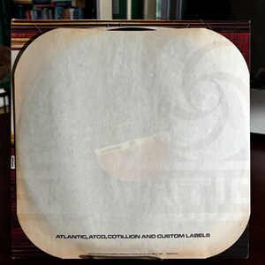 Op de afbeelding: Een vintage platenhoes met een witte binnenhoes. De hoes bevat de tekst "ATLANTIC, ATCO, COTILLION AND CUSTOM LABELS". Het album staat in een bruin en rood frame.