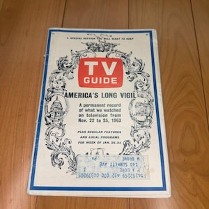 Pode incluir: Uma revista TV Guide vintage com capa branca, borda azul e logotipo vermelho. O texto diz: A SPECIAL SECTION YOU WILL WANT TO KEEP, TV GUIDE, AMERICA'S LONG VIGIL, A permanent record of what we watched on television from Nov. 22 to 25, 1963.