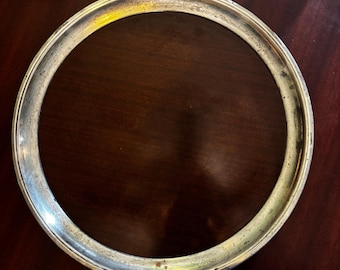 Peut inclure: Un cadre métallique circulaire de couleur argentée avec une surface légèrement texturée. Le cadre a un design simple et élégant et semble vieilli. Le fond est une surface en bois brun foncé.