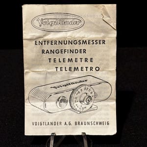 May include: A vintage Voigtländer rangefinder instruction sheet. The sheet features the Voigtländer logo and the words "ENTFERNUNGSMESSER RANGEFINDER TELEMETRE TELEMETRO". A line drawing of a rangefinder camera is also visible.