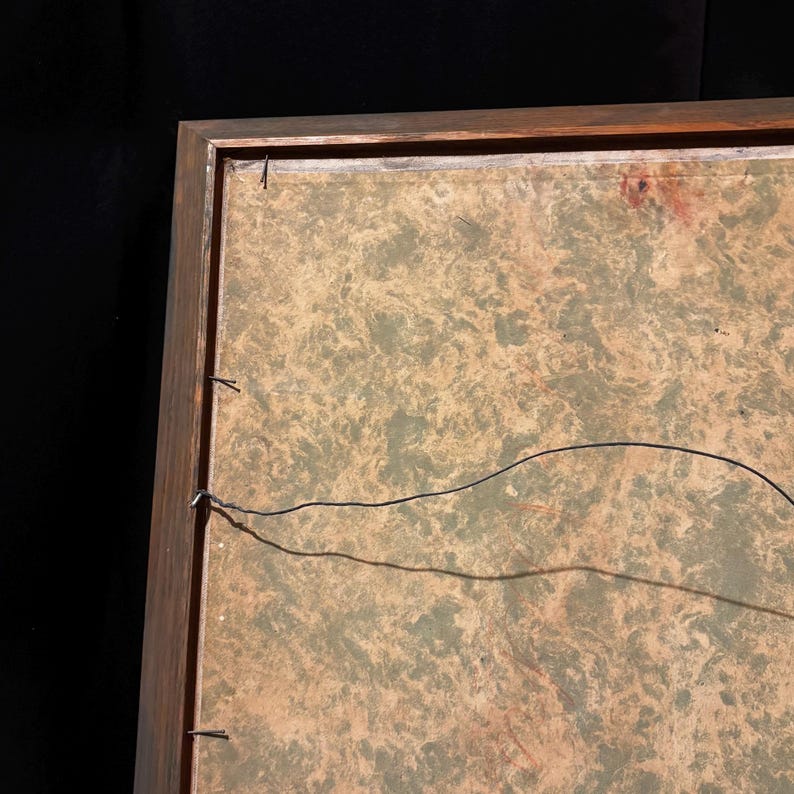 May include: A framed artwork with a wooden frame. The artwork has a mottled green and tan background. A black wire is strung across the back of the frame, secured with small nails. The frame is a dark brown color.