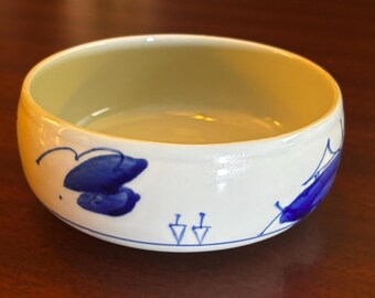 May include: A white ceramic bowl with a yellow interior and blue floral designs. The bowl has a rounded shape and a simple, elegant design. The blue floral designs are painted on the exterior of the bowl.