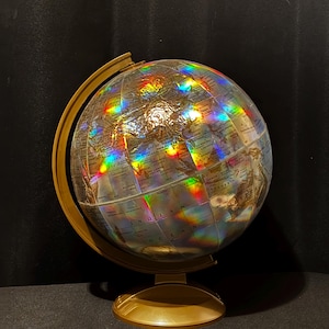 May include: A decorative globe with a gold-colored stand and meridian. The globe itself is clear with a holographic effect, displaying a rainbow of colors. The continents and oceans are labeled in a classic style.