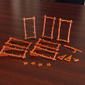 Puede incluir: Colección de piezas de valla de madera marrón en miniatura, puertas y elementos decorativos. El conjunto incluye secciones de valla rectangulares, puertas arqueadas y detalles en forma de estrella, todo en estilo rústico. También incluye pequeñas piezas decorativas marrones.