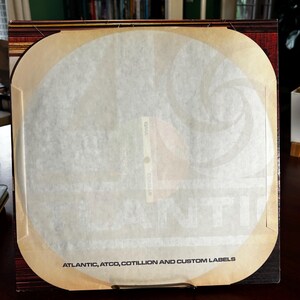 Op de afbeelding: Een vierkante platenhoes met een witte binnenhoes. De hoes is bruin met een beige rand en de tekst "ATLANTIC, ATCO, COTILLION AND CUSTOM LABELS" onderaan. De binnenhoes heeft een cirkelvormig ontwerp.