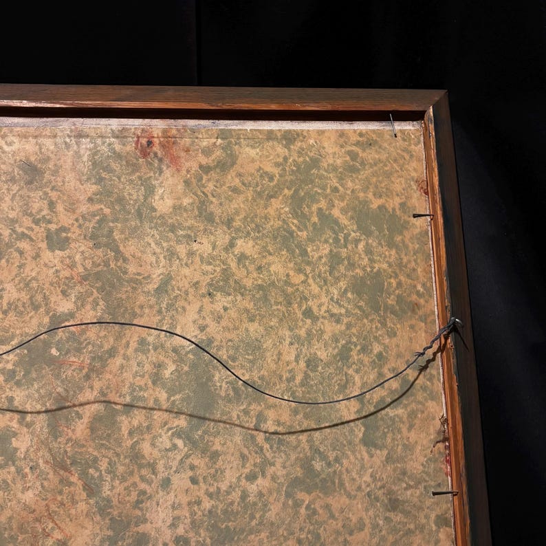 May include: Back of a framed artwork with a wooden frame. The artwork has a mottled green and tan background. A black wire is strung across the back for hanging. The frame is secured with small nails.