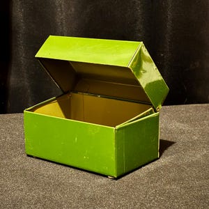 May include: A vibrant green metal box with a hinged lid, partially open. The box is rectangular with a glossy finish. The interior is a lighter shade of green. The box is likely for storage.