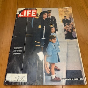 Pode incluir: Uma edição vintage da revista LIFE de 6 de dezembro de 1963 com uma fotografia de capa da Sra. Kennedy, Caroline e John Jr. em degraus de pedra. A capa inclui o texto branco: MRS. KENNEDY, CAROLINE AND JOHN JR. WAIT TO JOIN PROCESSION TO CAPITOL.