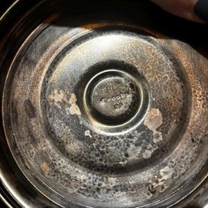 K&ouml;nnte beinhalten: Nahaufnahme des Bodens eines silberfarbenen Metallobjekts. In der Mitte befindet sich der Text "EPCA Crosby C2" in einem kreisf&ouml;rmigen Design. Das Metall hat ein strukturiertes, gealtertes Aussehen mit Verf&auml;rbungen.