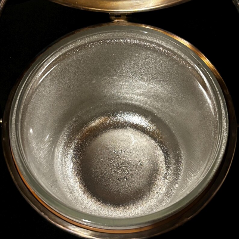 K&ouml;nnte beinhalten: Eine klare Pyrex-Glassch&uuml;ssel mit silbernem Metallrand und Griff. Die Sch&uuml;ssel hat einen strukturierten Innenraum, und das Pyrex-Logo ist unten sichtbar. Die Sch&uuml;ssel ist wahrscheinlich Teil eines Serviergeschirrs oder K&uuml;chenutensilien-Sets.