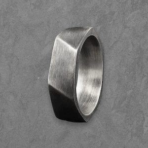 May include: A silver-toned ring with a geometric design. The ring has a flat top and sides, with a polished interior. The ring is made of metal and has a modern, minimalist style. The ring is approximately 1 inch in diameter.