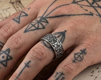 May include: A silver-toned metal ring featuring a repeating geometric pattern of small triangles across its entire outer surface. The band has a uniform width and a matte finish, showcasing a structured, angular design that encircles the finger.