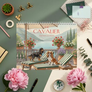 May include: A 2026 dog calendar featuring Cavalier King Charles Spaniels. The calendar shows two dogs on striped lounge chairs with a scenic background. The title "The Cavalier" is displayed in red.