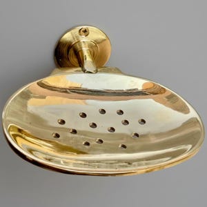 Angled view of brass soap holder mounted on wall, showing smooth oval design and artisan shine.