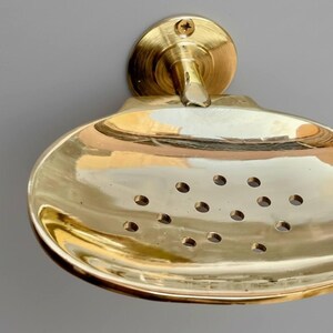 Front view of solid brass wall soap dish highlighting drainage holes and reflective golden surface.