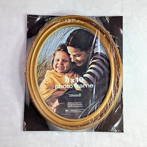May include: An oval-shaped gold-colored plastic photo frame measuring 8 by 10 inches. The frame is encased in clear plastic packaging and features a display image of a child and an adult. The text on the display reads 8 x 10 photo frame.