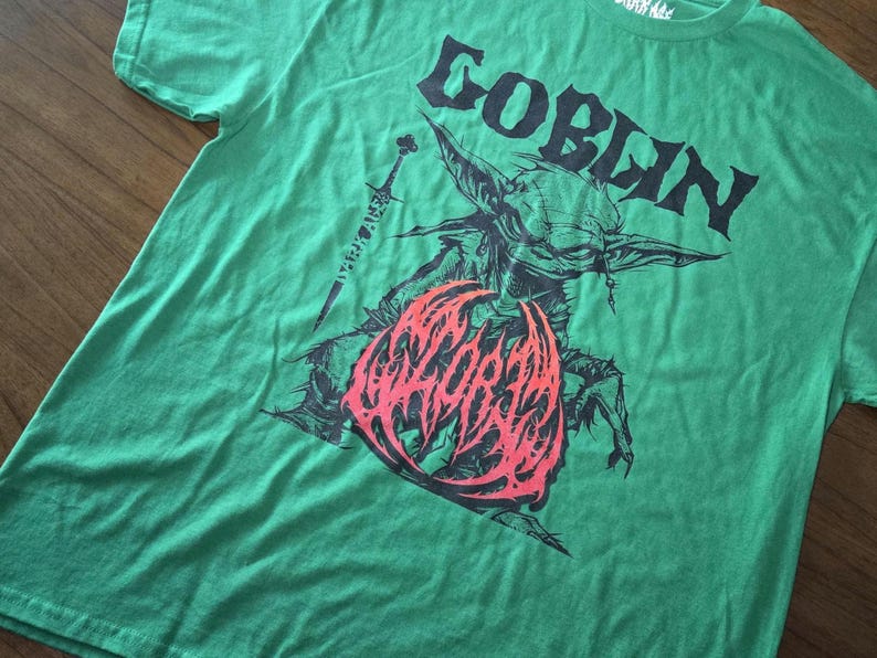 May include: Green t-shirt with a graphic of a goblin, a sword, and the word "GOBLIN" in black. The goblin graphic has red and black accents. The shirt is made of a soft material.