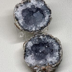 Puede incluir: Una caja geoda con bisagras que presenta dos mitades circulares forradas con cristales de amatista de color p&uacute;rpura intenso. El exterior de la roca es una piedra marr&oacute;n rugosa y texturizada. Una peque&ntilde;a bisagra de metal plateado conecta las dos mitades, lo que permite que la geoda se abra y cierre como un recipiente.