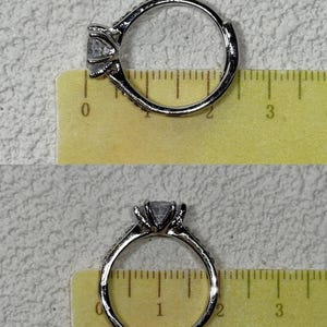 Puede incluir: Un anillo de tono plateado con una piedra transparente facetada en un engaste de garras. El anillo est&aacute; colocado sobre una regla amarilla que muestra un di&aacute;metro de aproximadamente 1,9 cm. La banda tiene peque&ntilde;as piedras incrustadas.