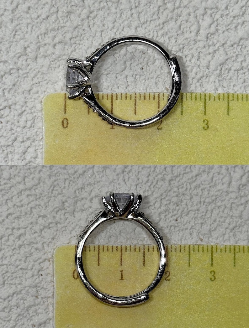 Puede incluir: Un anillo de tono plateado con una piedra transparente facetada en un engaste de garras. El anillo est&aacute; colocado sobre una regla amarilla que muestra un di&aacute;metro de aproximadamente 1,9 cm. La banda tiene peque&ntilde;as piedras incrustadas.