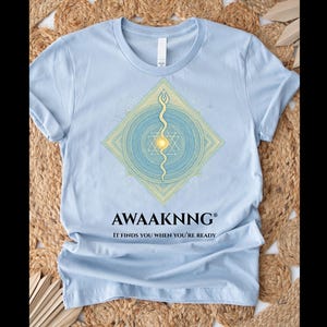 Camiseta Despertar Espiritual, azul claro, calidad premium, diseño de geometría sagrada para manifestación y fuerza interior, marca registrada AWAAKNNG