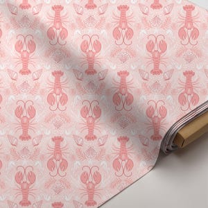 May include: Pink fabric with a repeating pattern of lobsters, seashells, and seahorses. The design features coral-colored lobsters and white seashells and seahorses on a light pink background. The fabric is rolled up on a cardboard tube.