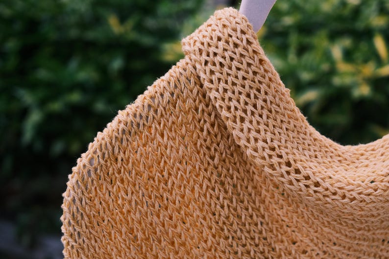 Puede incluir: Primer plano de una tela de punto beige de tejido abierto. La textura es visible, con un patr&oacute;n de diamantes repetido. La tela parece ser parte de una prenda, posiblemente un chal o una bufanda.
