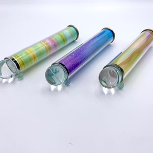 May include: Three glass kaleidoscopes with different colored designs inside. The kaleidoscopes are clear glass with silver caps on each end.