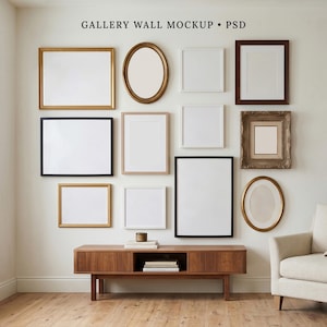 May include: A gallery wall mockup featuring eleven assorted empty picture frames in various shapes, sizes, and colors, including gold, black, white, and wood tones, arranged on a wall above a wooden media console with books and a small object.