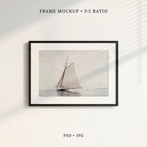 May include: A black rectangular frame containing a print of a sailboat on water, with the text FRAME MOCKUP 3:2 RATIO at the top and PSD JPG at the bottom. The sailboat has white sails and is positioned on a calm, light-colored sea under a hazy sky.
